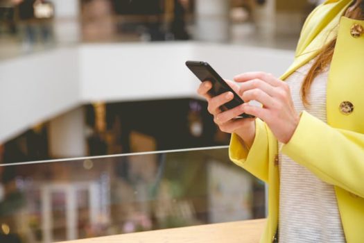mulher de casaco amarelo com o telefone na mão em um shopping center