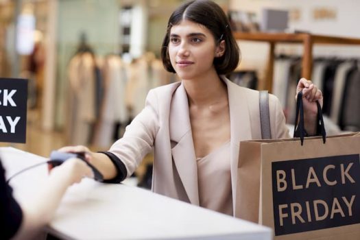 Mulher fazendo compras em uma loja de roupas. Em suas mãos, uma sacola de papel com "Black Friday" escrito.